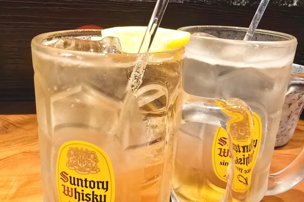 Two large glass mugs filled with iced Suntory Whisky highballs garnished with lemon slices and straws, served at a Japanese dining bar.