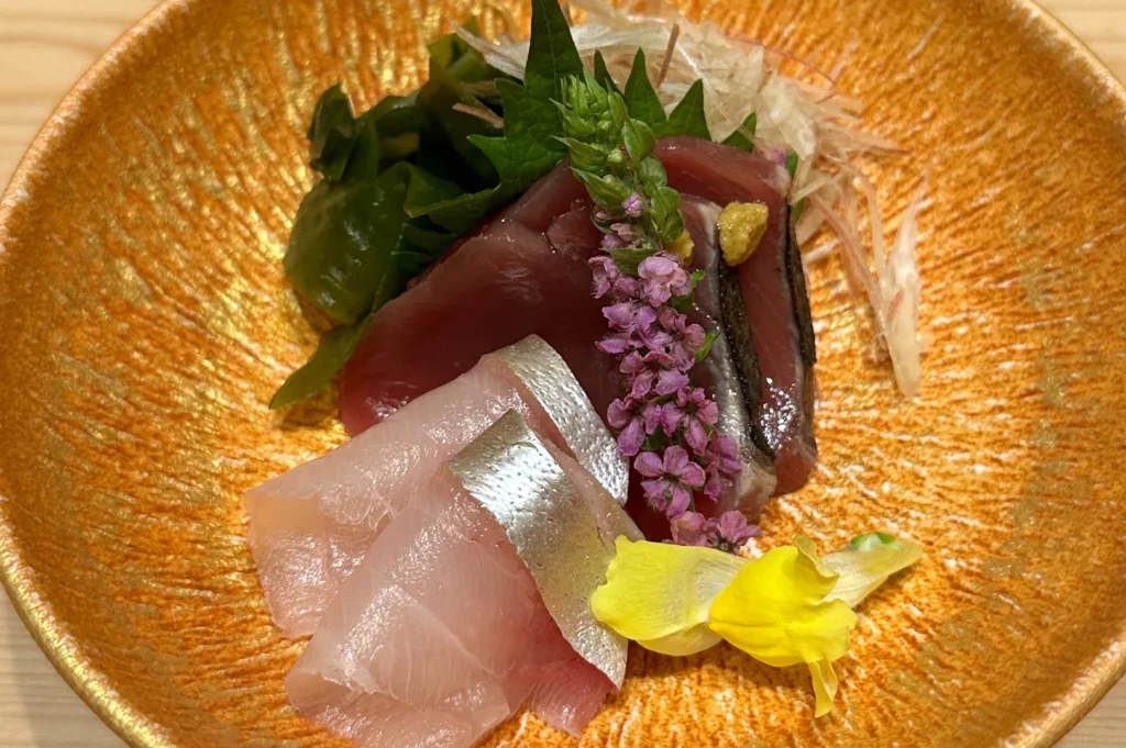 Exquisite sashimi platter featuring tuna and yellowtail garnished with edible flowers and shiso leaves at Shinji by Kanesaka, St. Regis Singapore.