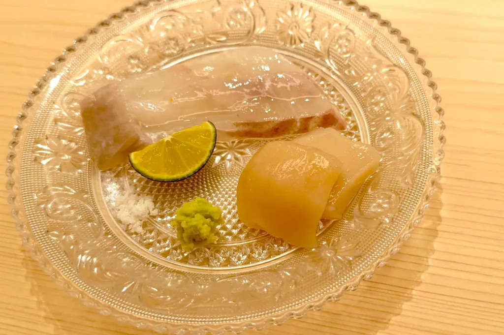 Freshly sliced pine flounder served on an intricate glass plate with yuzu kosho, wasabi, and sea salt at Sushi Sakuta.