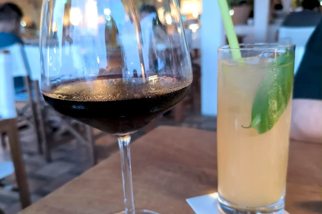 A chilled glass of red wine alongside a refreshing cocktail garnished with a fresh basil leaf on a wooden table at Fico Singapore.
