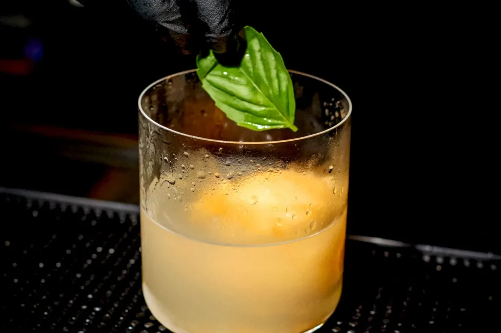 A hand in a black glove garnishing the signature Cantaloop Rush drink, made with rock melon sorbet and gin, with a fresh green mint leaf at Rasa Space.