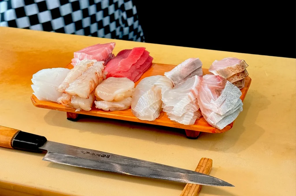 A variety of fresh, expertly sliced sashimi arranged on a wooden board next to a Japanese chef's knife at Ryo Sushi, Orchard Hotel, Singapore.