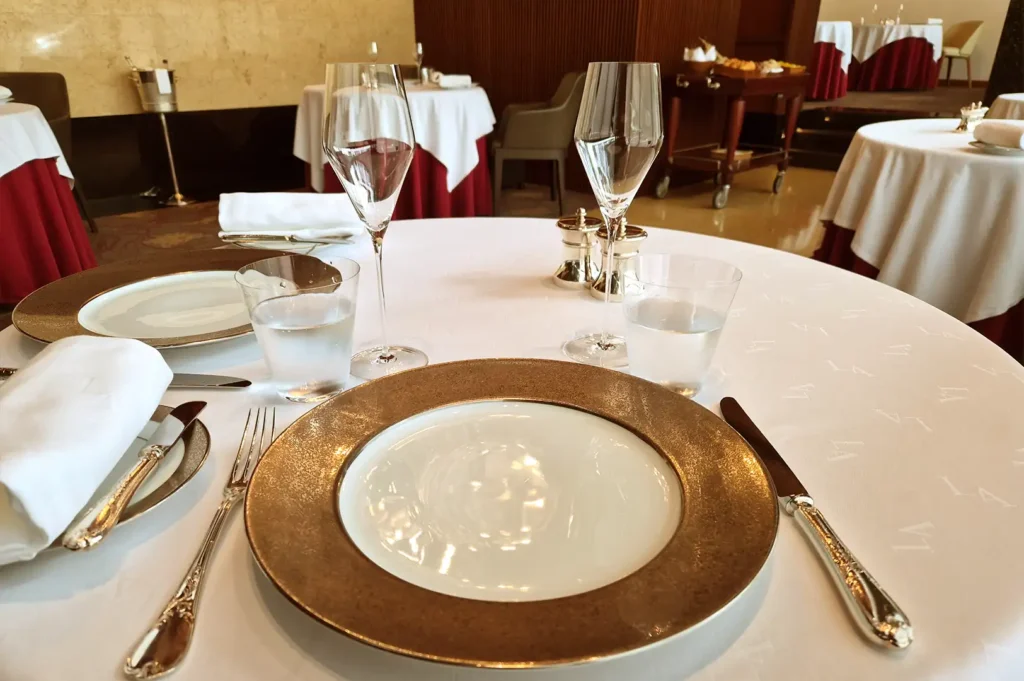 A beautifully set fine dining table in Singapore with a white tablecloth, gold-rimmed charger plate, crystal wine glasses, and polished silverware.