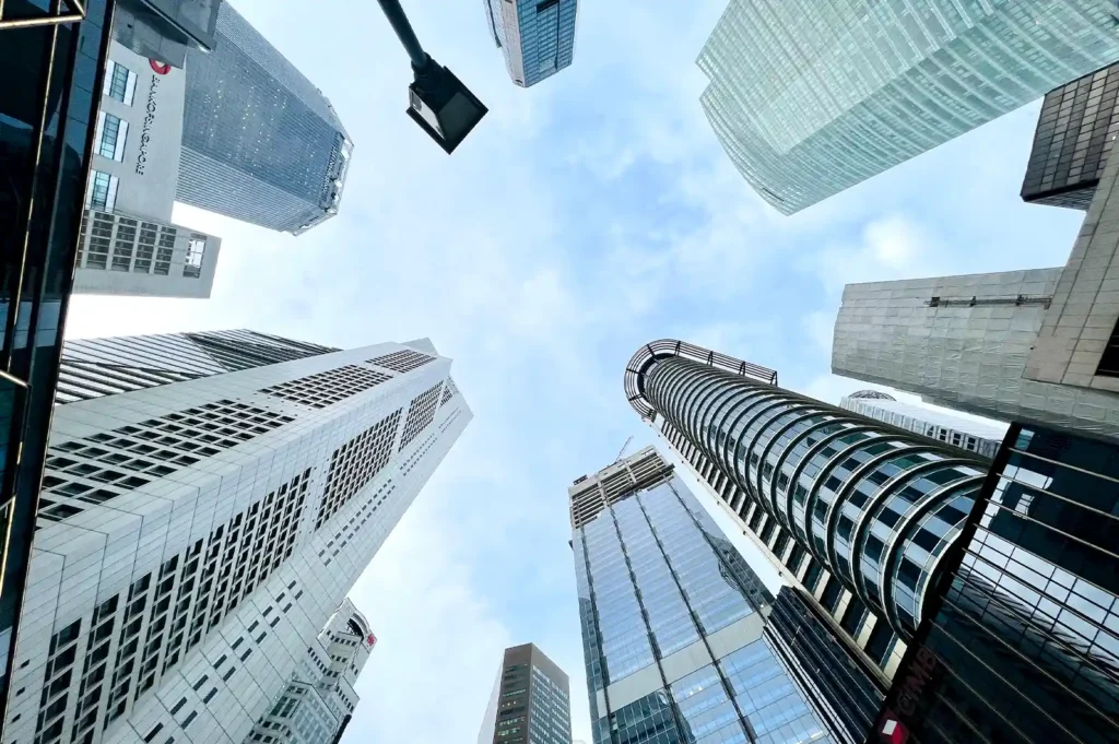 A low-angle upward view of towering commercial skyscrapers against a bright blue sky in the Raffles Place central business district.