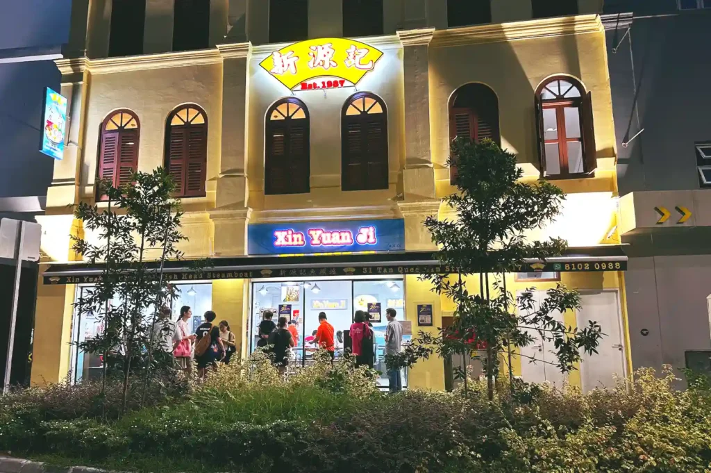 Exterior view of the brightly lit Xin Yuan Ji restaurant storefront at night, showcasing its traditional shophouse architecture and signage on Tan Quee Lan Street in Singapore.