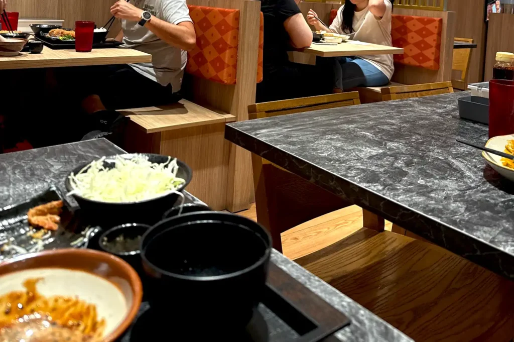 Interior view of the dining area at Gochi-So Shokudo showing customers seated at wooden tables with orange cushioned booths.