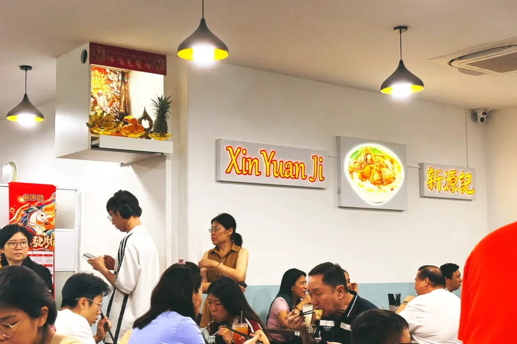 Busy and welcoming indoor dining atmosphere filled with customers enjoying classic Singapore-style fish soup under warm pendant lighting at Xin Yuan Ji.