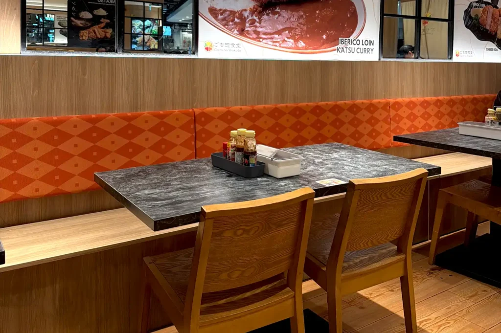 Cozy dining booths with marble-top tables, orange patterned cushions, and condiments neatly arranged at Gochi-So Shokudo.