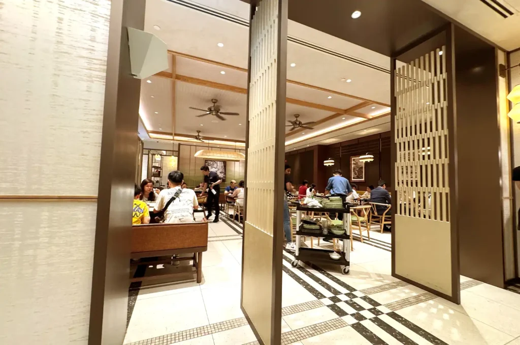 A wide view of the modern, cozy dining area at Tim Ho Wan PEAK with patrons enjoying their meals and staff attending tables.