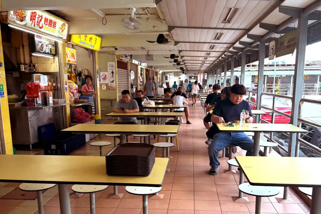 Wide-angle view of the covered outdoor dining area and food stalls at Havelock Road Cooked Food Centre with seated patrons enjoying their meals.