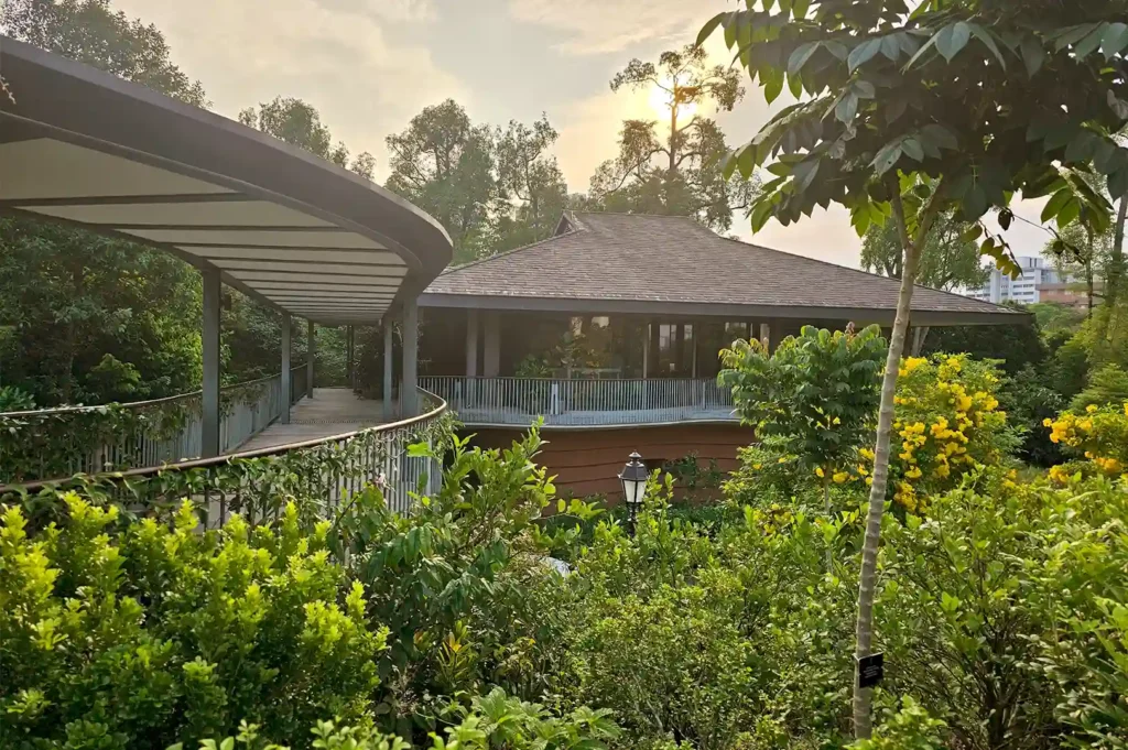 The lush exterior and covered walkway of Pangium in Singapore, showcasing a serene garden dining setting surrounded by tropical greenery.