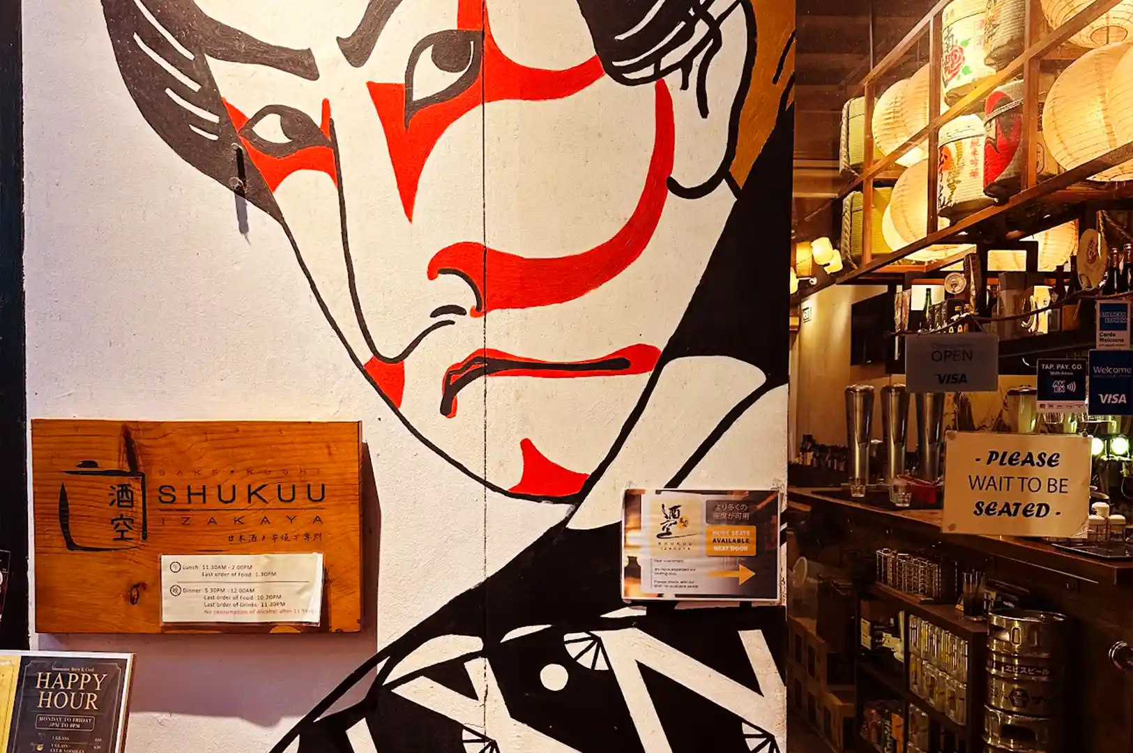 Entrance wall of ShuKuu Izakaya featuring a large Kabuki character mural alongside wooden signboards and hanging paper lanterns on Stanley Street.