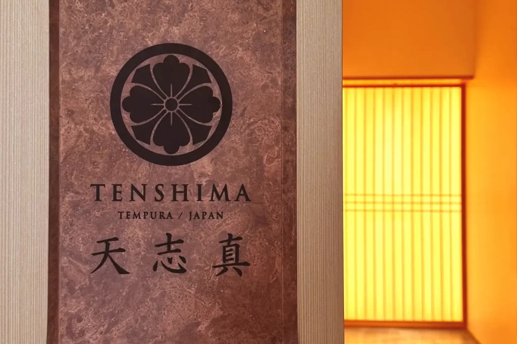 The entrance plaque and warm wooden doorway of Tenshima, a specialized fine dining tempura restaurant in Japan.