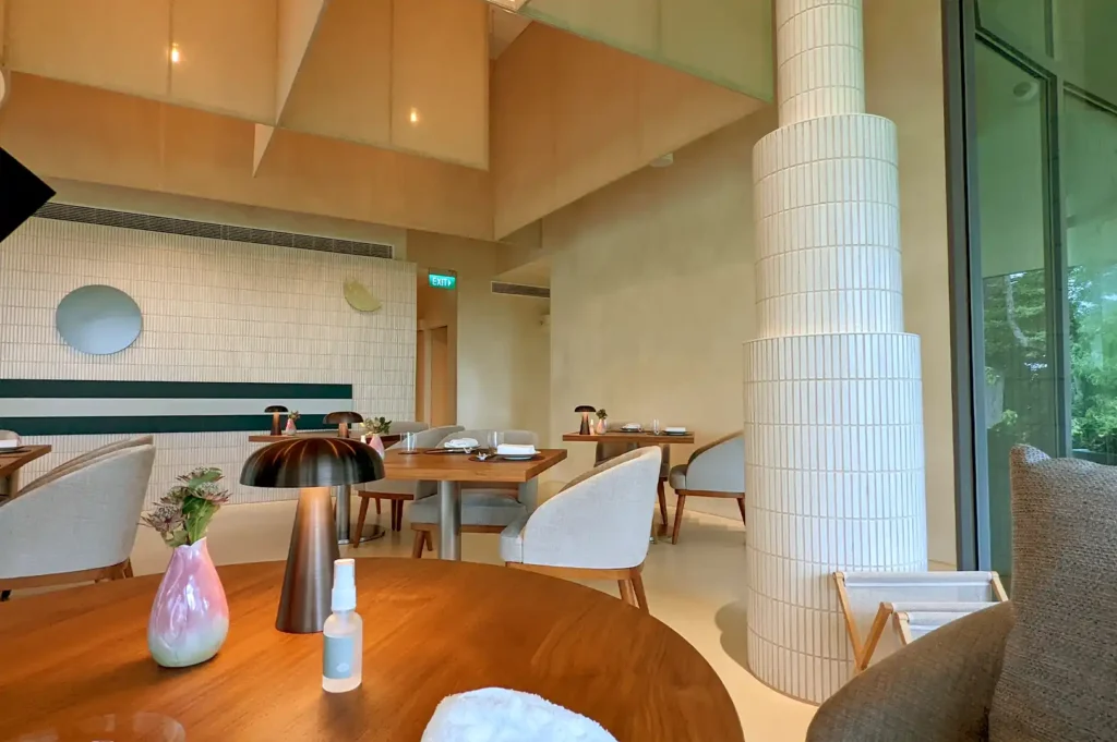 The elegant, modern interior of Pangium featuring warm lighting, minimalist wooden furniture, and floor-to-ceiling glass windows overlooking the surrounding foliage.