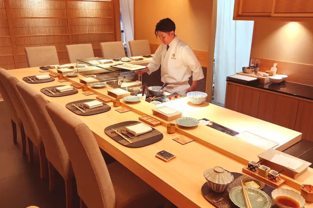 The intimate ten-seat wooden counter dining setup at Tenshima, where a chef prepares refined dishes around the hot oil.