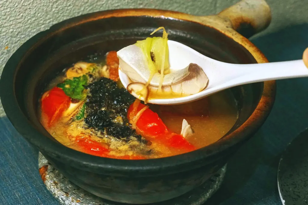 A ceramic spoon lifting a tender slice of fresh pomfret fish from a steaming claypot soup at Hup Lok.