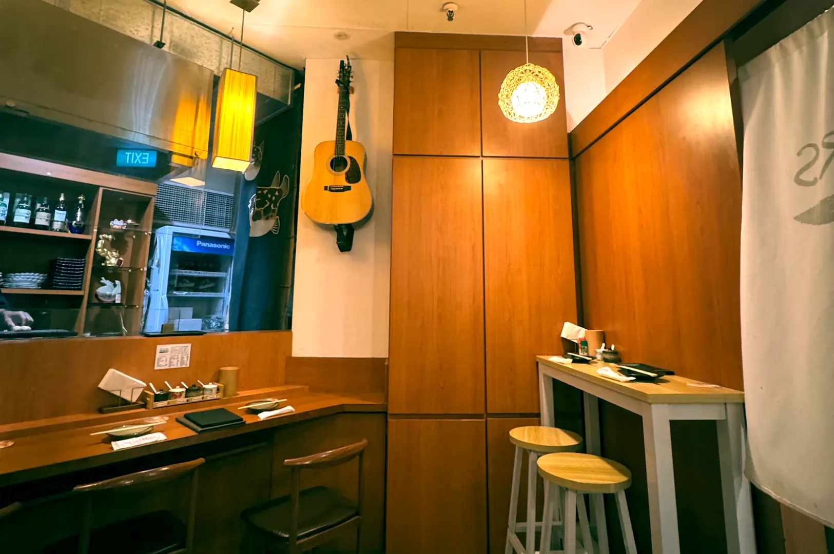 Cozy interior corner of Skewers Yakitori Izakaya featuring high table seating, warm wooden paneling, and an acoustic guitar mounted on the wall.