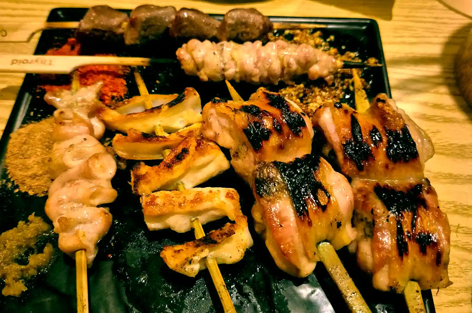 Platter of assorted charcoal-grilled yakitori chicken skewers served with chili powders and seasonings at Skewers Yakitori Izakaya.