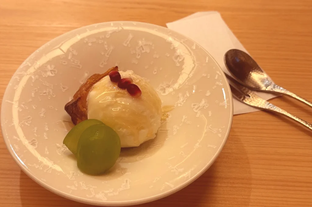 A gourmet dessert at Tenshima featuring sweet potato tempura paired with a scoop of ice cream, drizzled with honey, and garnished with fresh fruit.
