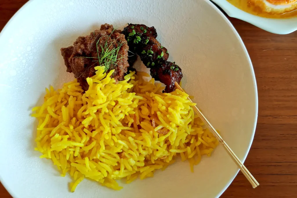 A vibrant platter of aromatic Nasi Ulam served alongside tender oxtail satay, capturing the depth of Peranakan culinary heritage.