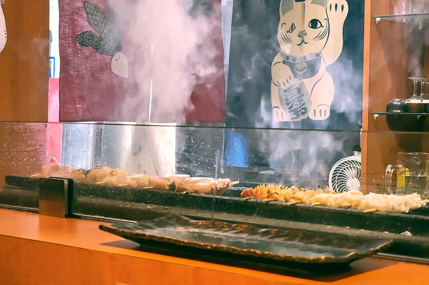 Left: A single grilled Chicken oyster skewer with crispy charred skin served on a ceramic plate; Right: Platter of various chicken skewers including liver and heart.