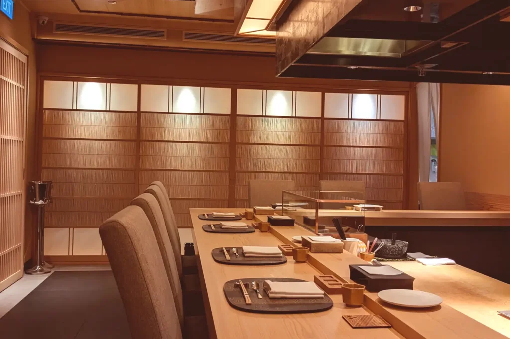 A wide-angle view of the elegant, minimalist dining interior at Tenshima, highlighting traditional shoji screen walls and the exclusive counter surrounding the central cooking station.