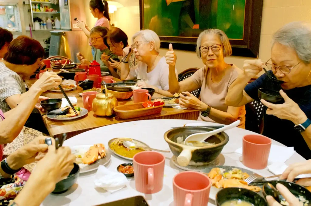 A group of diners smiling and giving a thumbs-up while sharing a table full of comforting Singaporean seafood dishes, pomfret soup, and prawn noodles at Hup Lok.