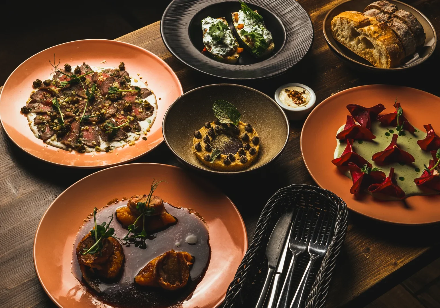 16 Singapore Best Restaurants Revamp Overhead shot of gourmet fine dining table with six artfully plated dishes including sliced meat, roasted vegetables, sauces, bread, and garnishes, showcasing culinary artistry.